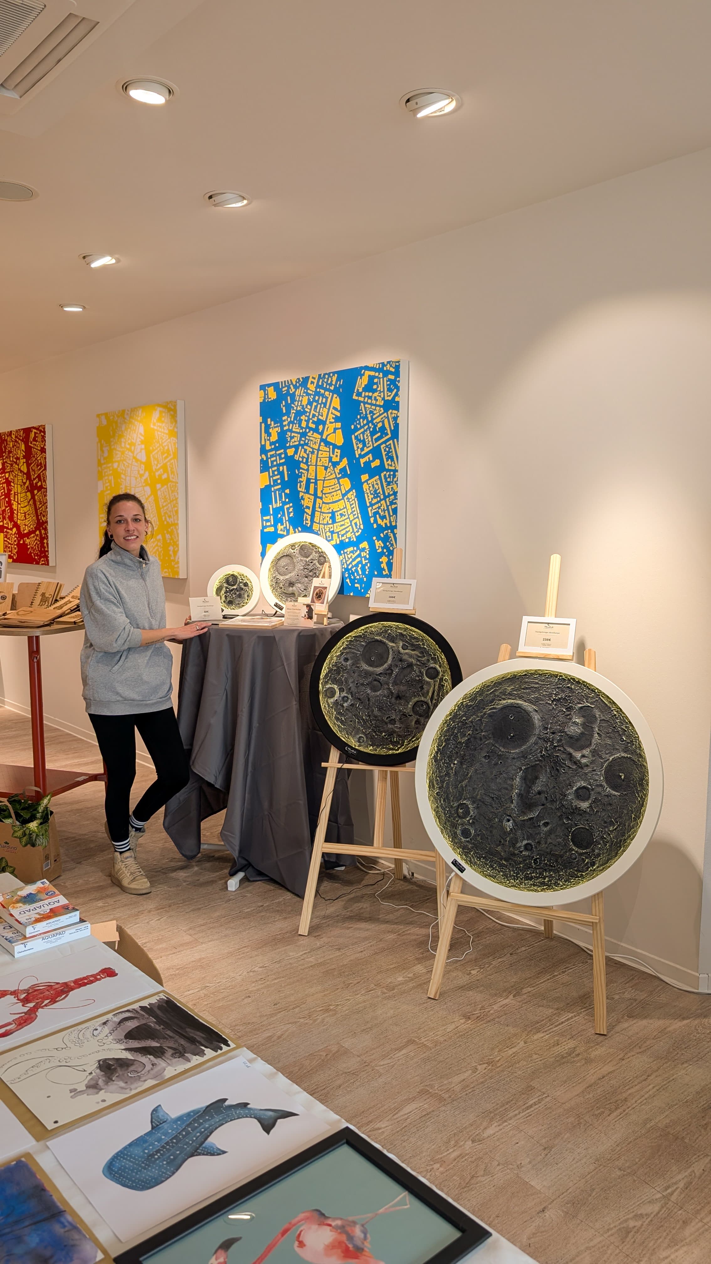 Eine Frau posiert in einer Galerie mit großen, strukturierten kreisförmigen Mondkunstwerken auf hölzernen Staffeleien.