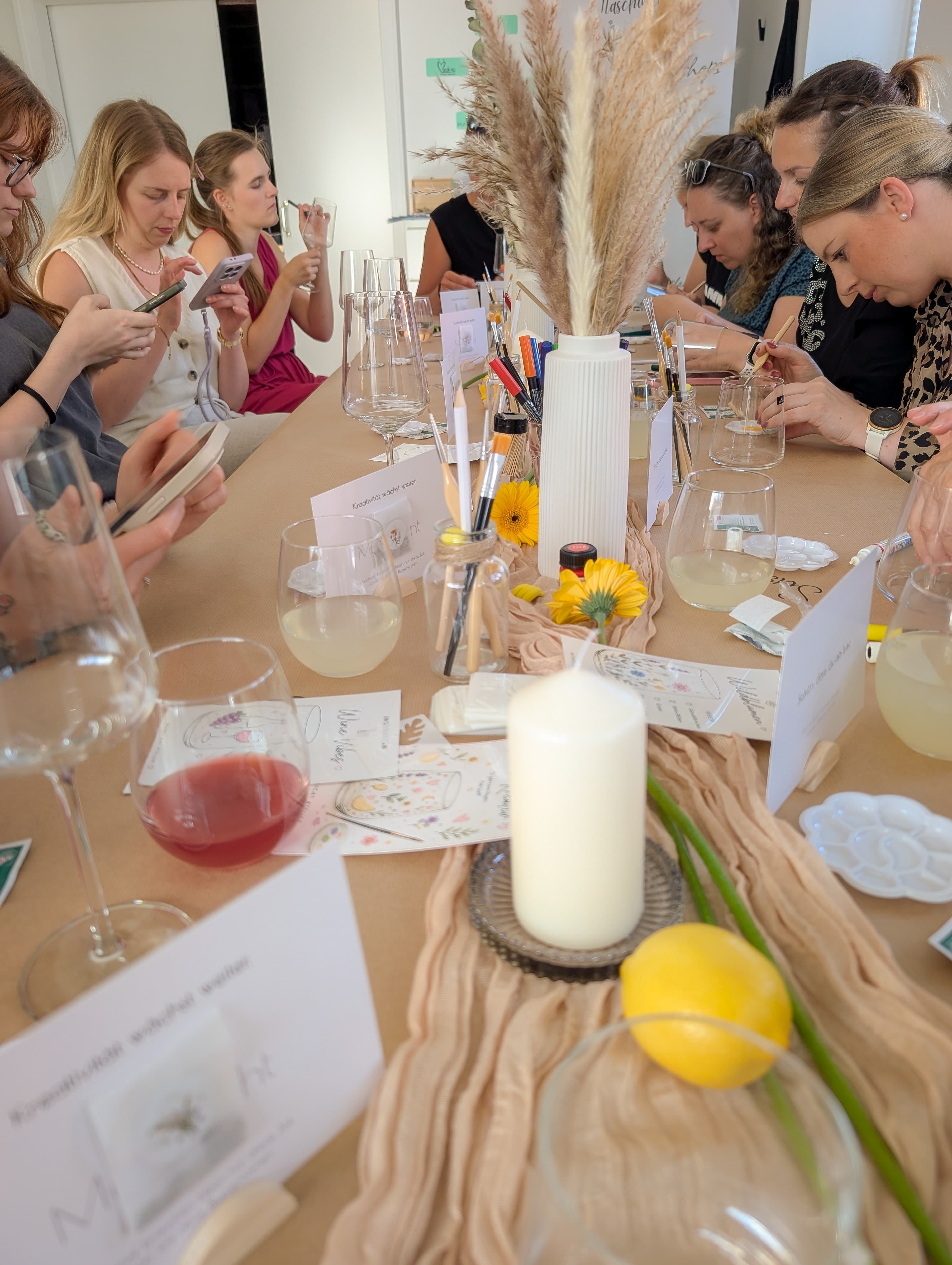 Frauen sitzen an einem festlich dekorierten Tisch und nehmen an einem kreativen Mal-Workshop teil.