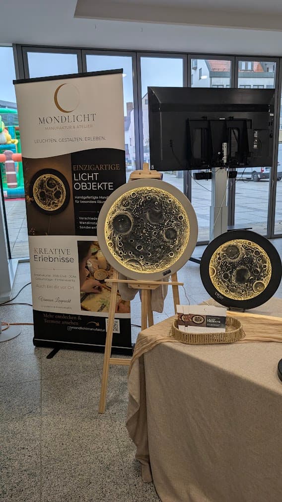 Werbestand der Mondlicht Manufaktur mit kunstvoll leuchtenden Mond-Lichtobjekten auf einer Staffelei und einem Tisch.